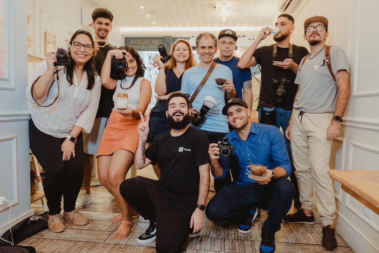 A diverse group of photographers holding cameras, smiling and posing indoors.